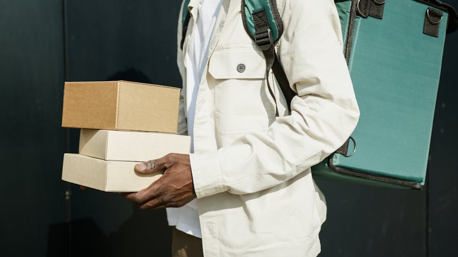 A person wearing a white jacket and carrying a teal backpack holding three rectangular boxes, possibly flower arrangements or deliveries, in front of a dark background, with no flowers visible in this